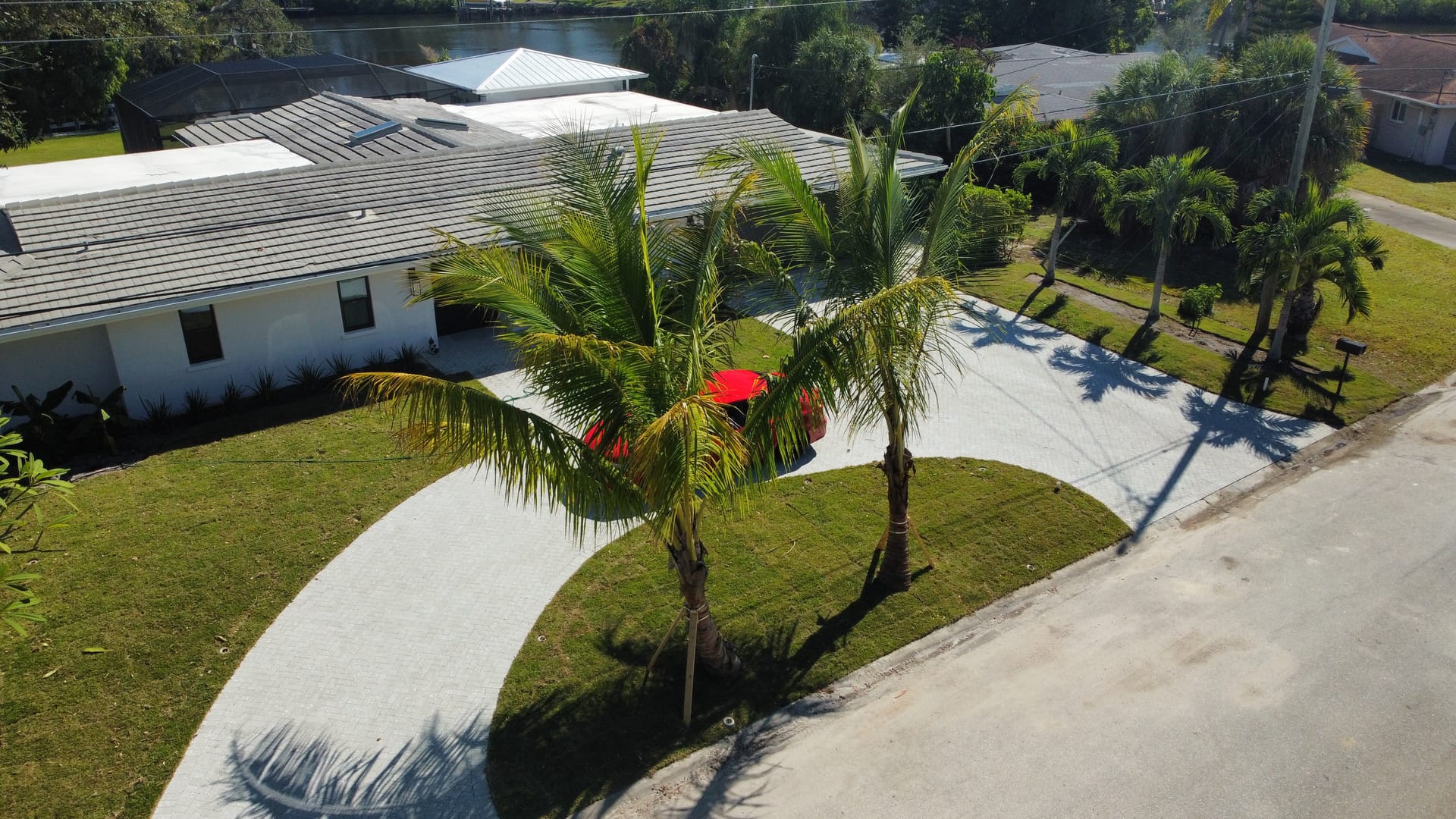 Waterfront home with curved paver driveway and young palm trees