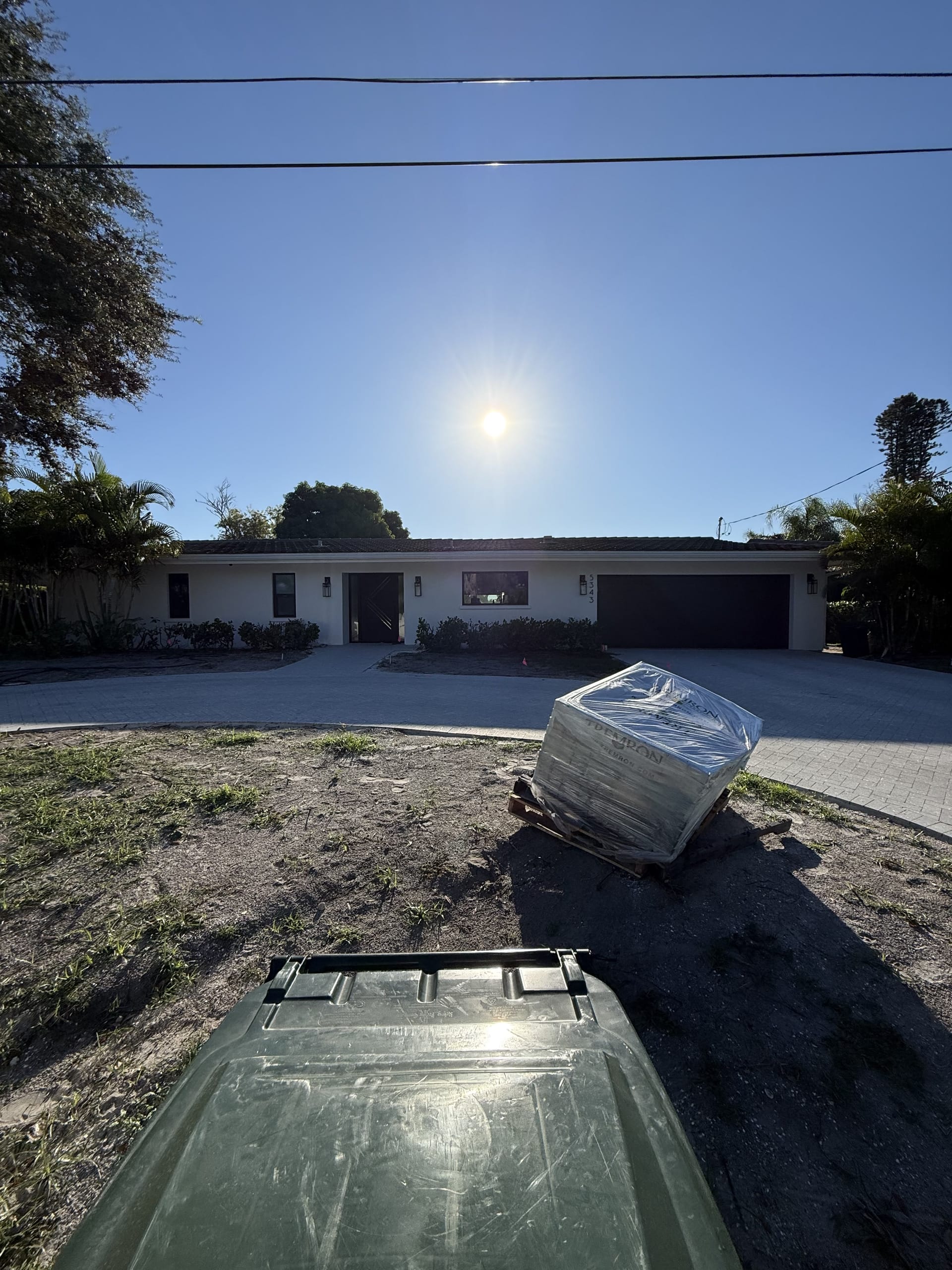 Before: the same white ranch home mid-project, with paver pallets on the lawn